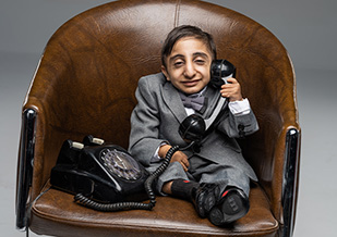 worlds shortest man sat on brown chair holding phone to ear